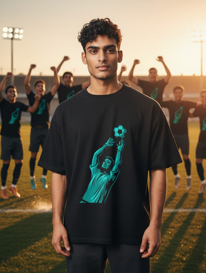 Print 999 black cotton graphic t-shirt featuring a teal goalkeeper save illustration, worn by a man on a soccer field.