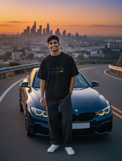 Print 999 black oversized cotton t-shirt with neon car graphic worn by a man standing before a car at sunset