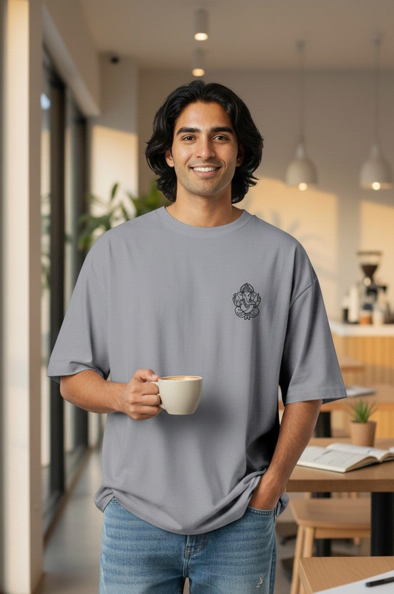 Print 999 grey oversized heavyweight cotton t-shirt with Ganesha line art, worn by a smiling man in a cafe.