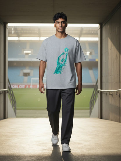 Print 999 grey cotton graphic t-shirt with a teal soccer goalkeeper print worn by a man in a stadium tunnel.
