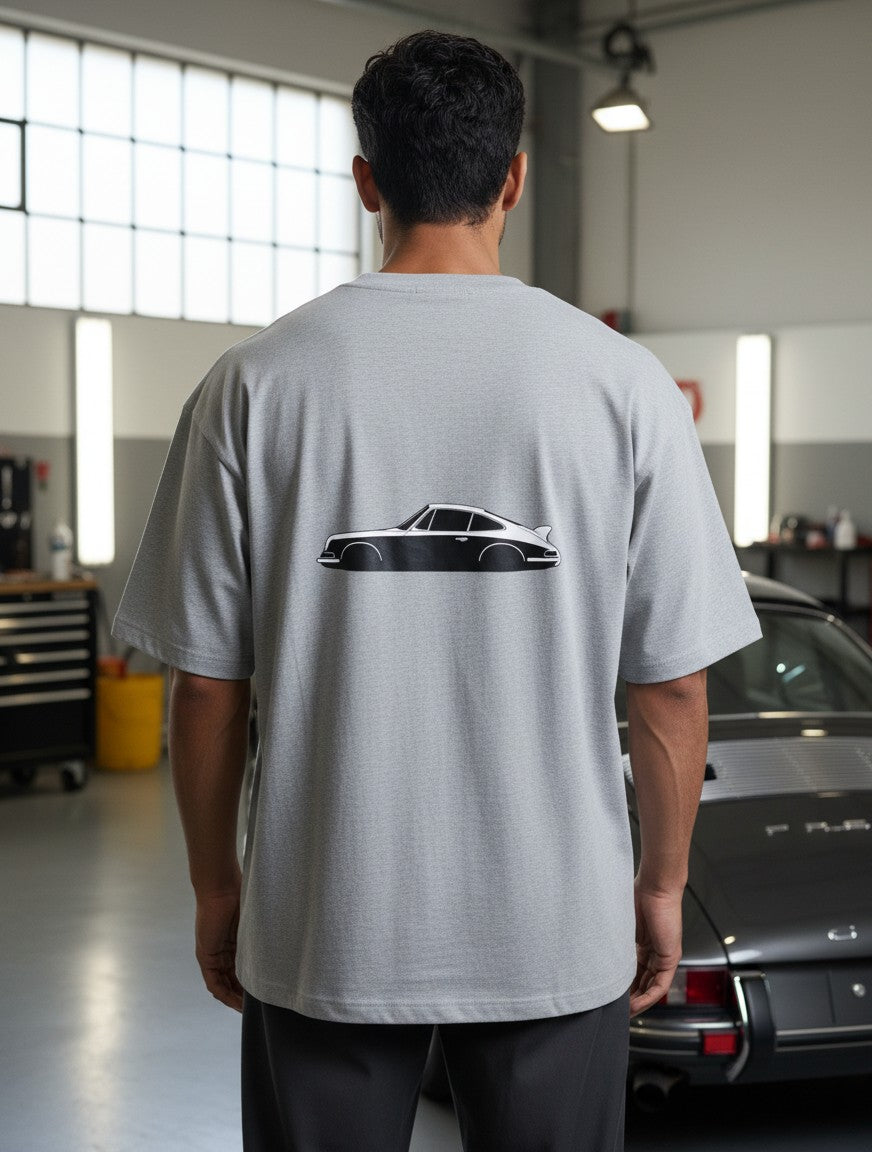 Print 999 grey oversized t-shirt with a vintage car graphic on the back, worn by a man in a garage setting.