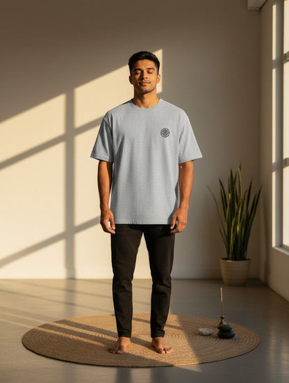 Print 999 grey oversized t-shirt with embroidered Om Sri Yantra emblem worn by a man in a sunlit room.
