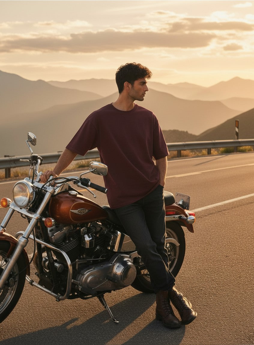 Print 999 oversized maroon cotton biker t-shirt worn by a man leaning against a motorcycle at sunset on a mountain road