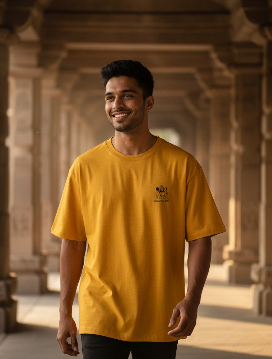 Print 999 mustard yellow oversized t-shirt with a small Hanuman Ji chest emblem worn by a smiling man in a temple.
