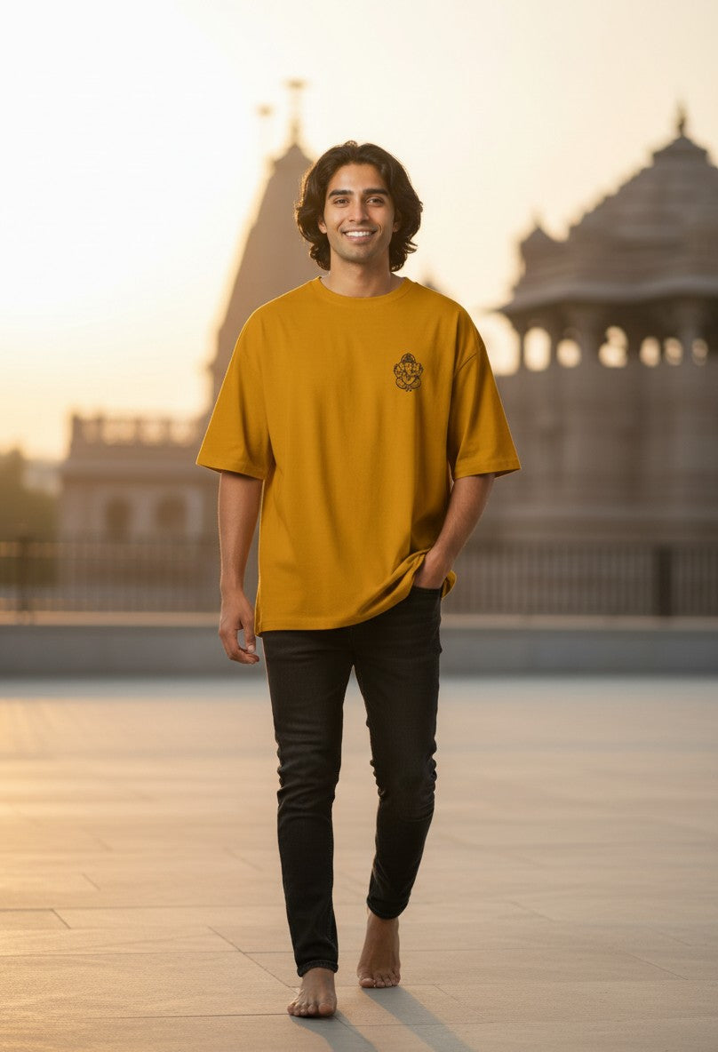 Print 999 mustard yellow oversized cotton t-shirt with Ganesh line art, worn by a man at a temple at sunset.