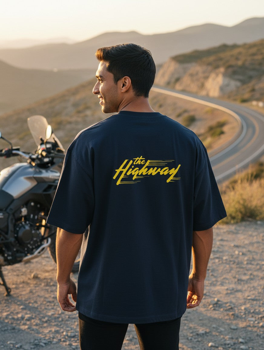 Print 999 navy oversized cotton t-shirt with yellow The Highway graphic on back, worn by a man near a motorcycle.