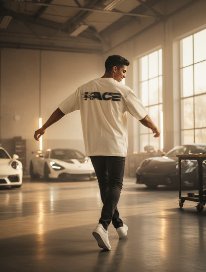 Print 999 oversized cream t-shirt with black Race graphic on back, worn by a man in a garage with sports cars.