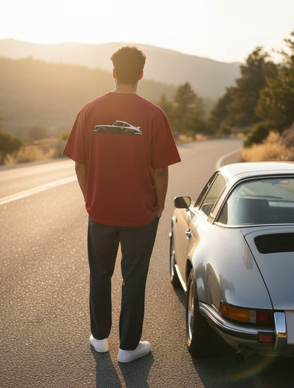 Print 999 Vintage Velocity oversized red t-shirt with car graphic on back worn by man standing by a vintage car