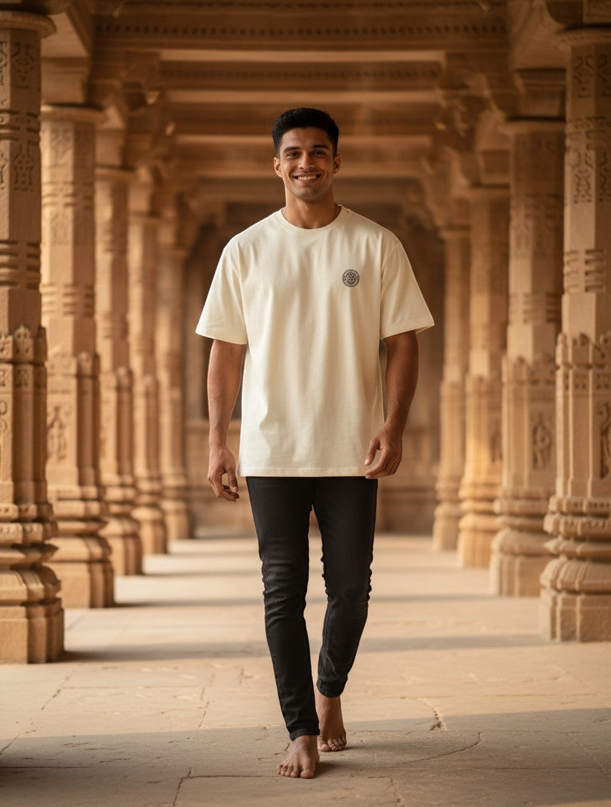 Print 999 oversized cream t-shirt with embroidered Sri Yantra emblem worn by a man in a temple corridor.