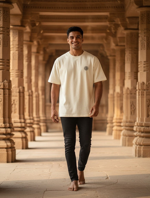 Print 999 oversized cream t-shirt with embroidered Sri Yantra emblem worn by a man in a temple corridor.