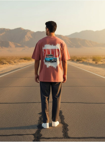 Print 999 oversized terracotta cotton t-shirt with Run Wild vintage car graphic, worn by a man on a desert road.