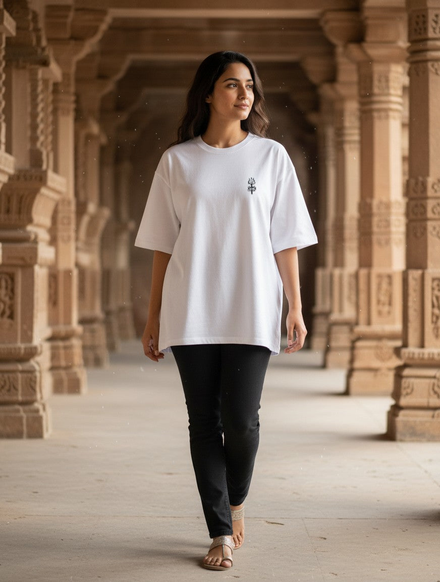 Print 999 white oversized cotton t-shirt with embroidered Trishul emblem worn by a woman in a temple corridor.